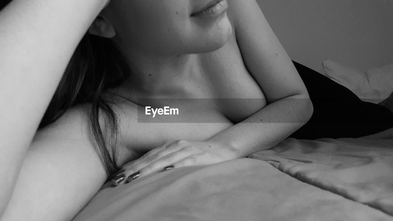 Midsection of sensuous young woman covering breasts with hand while lying on bed