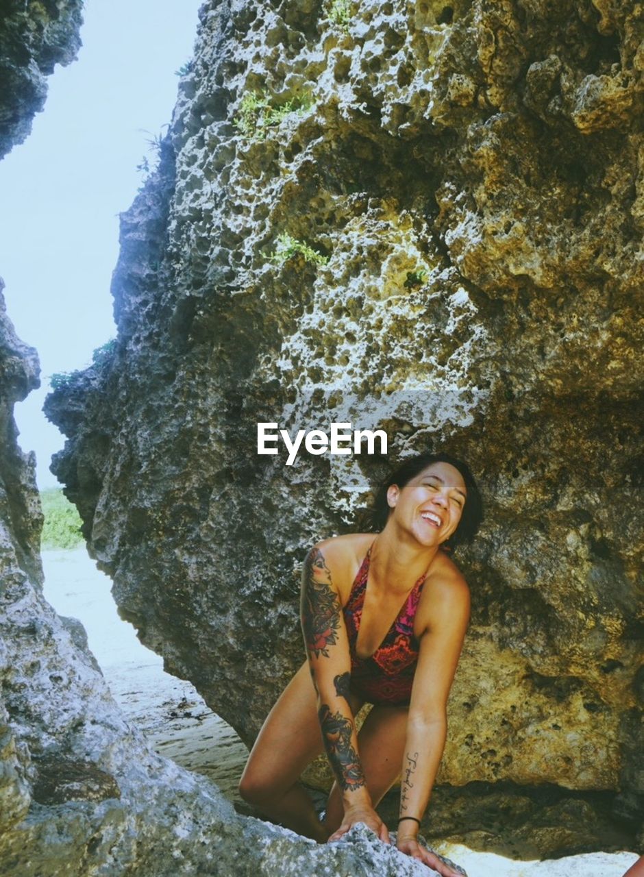 Smiling woman in swimsuit kneeling on rock at beach