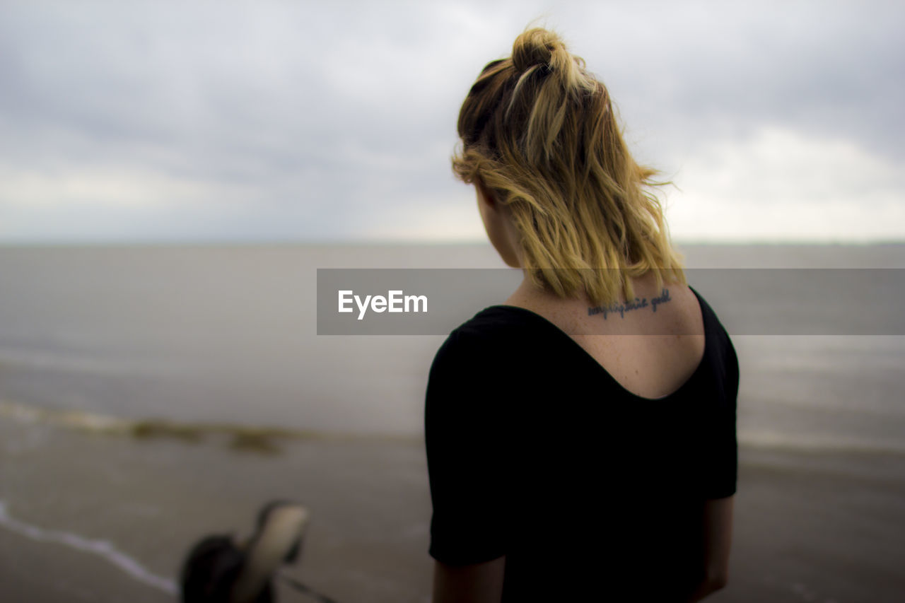 Rear view of woman standing at beach against sky