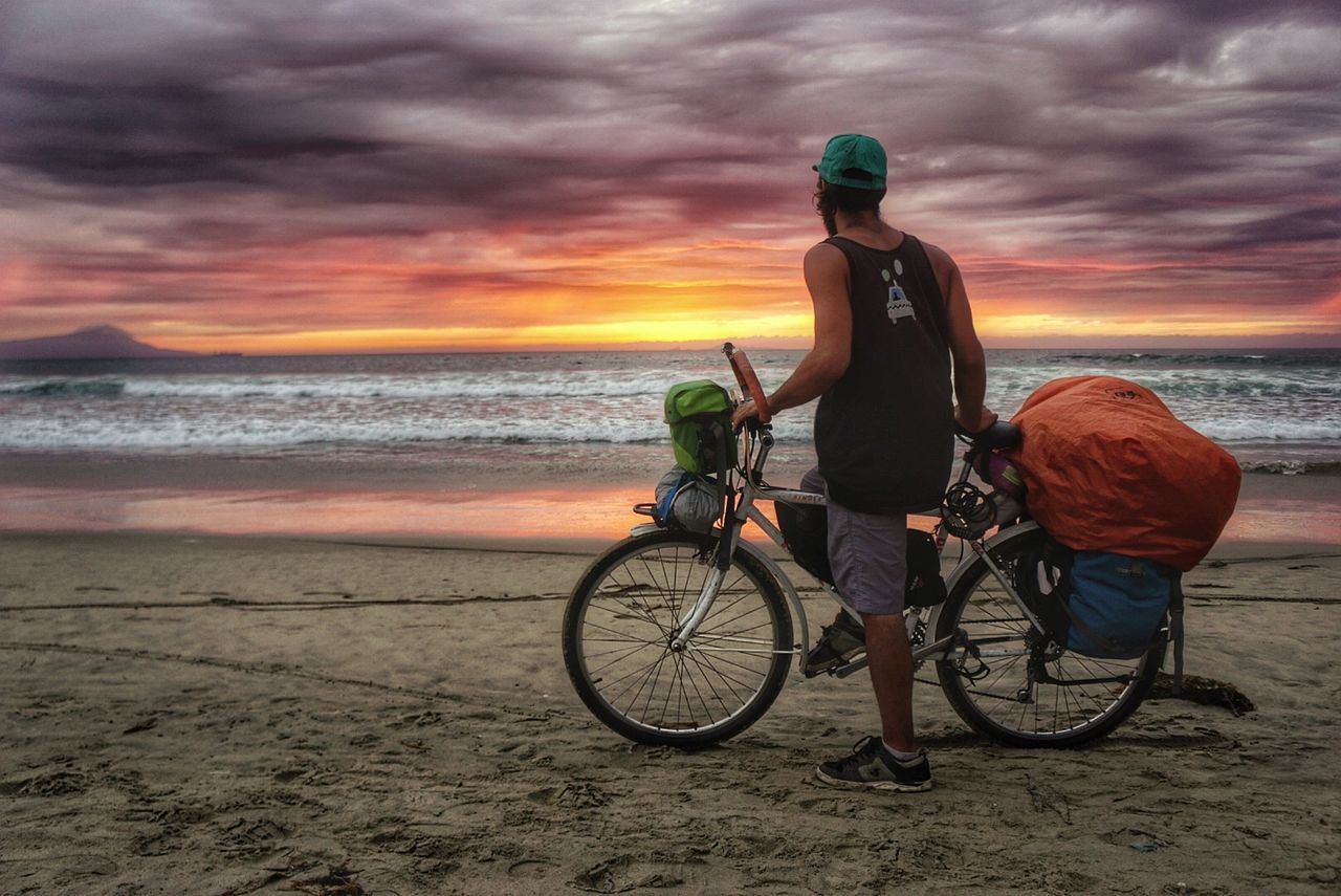 MAN SITTING ON BICYCLE AT BEACH