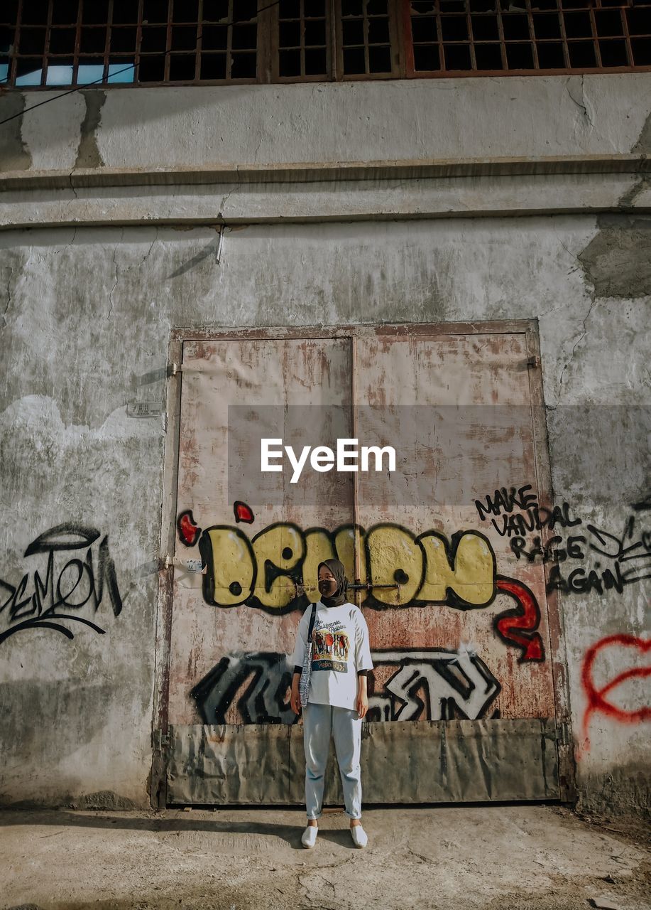 MAN STANDING BY GRAFFITI ON WALL