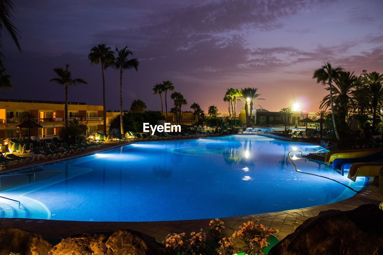 SWIMMING POOL BY TREES AGAINST SKY AT NIGHT