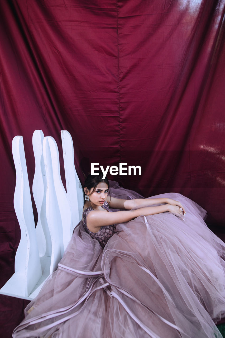 High angle portrait of woman wearing dress sitting against curtain