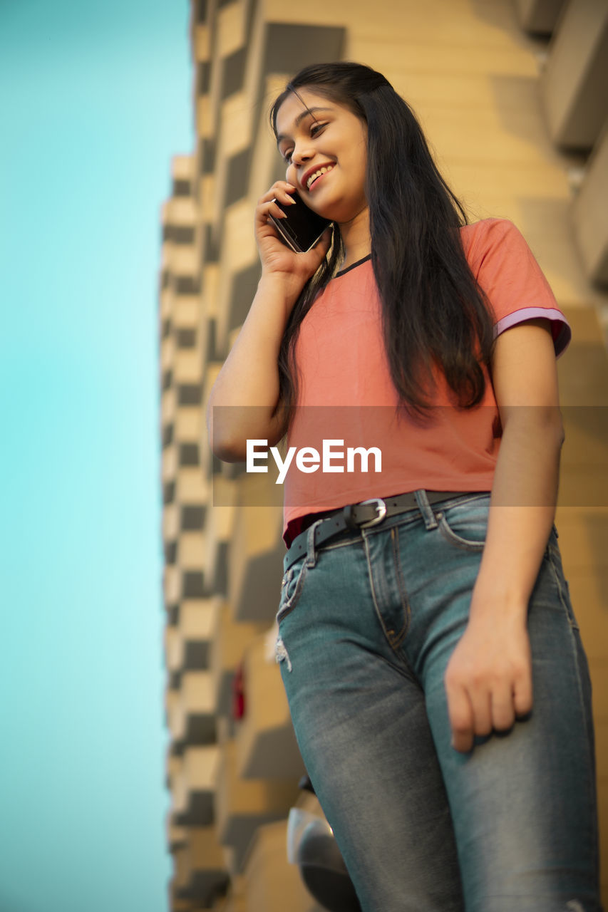 young woman looking away while standing against wall