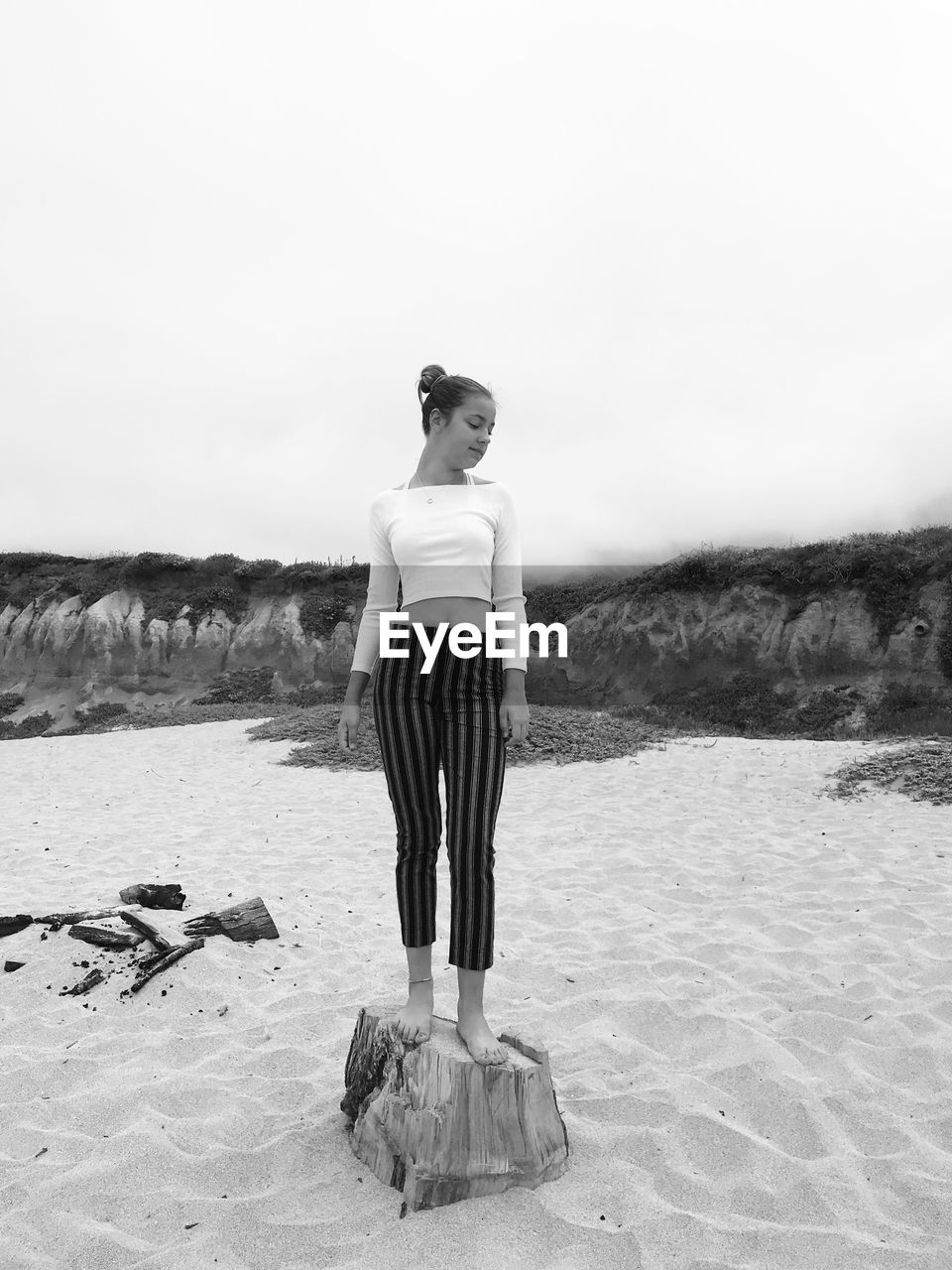 Full length of girl standing on tree stump at beach against sky