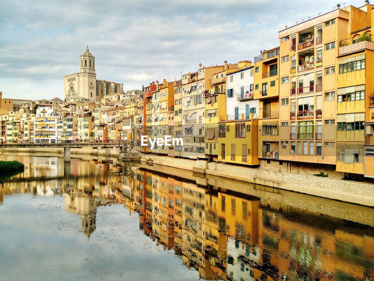 Buildings reflecting on calm river against cloudy sky 