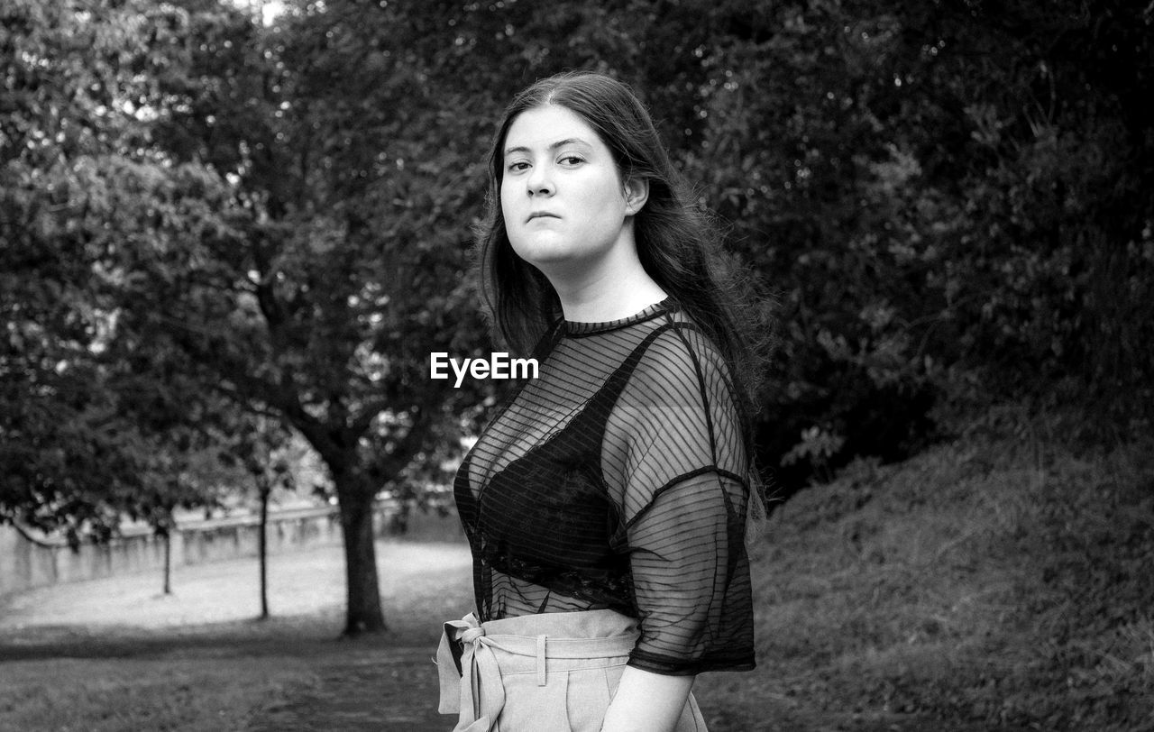 Portrait of beautiful young woman standing against trees