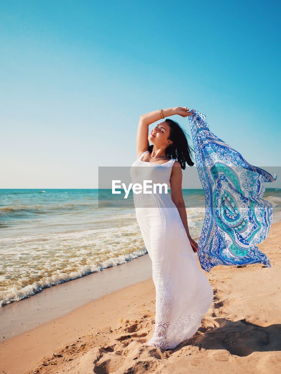 Full length of woman holding scarf on shore against sky at beach during sunny day