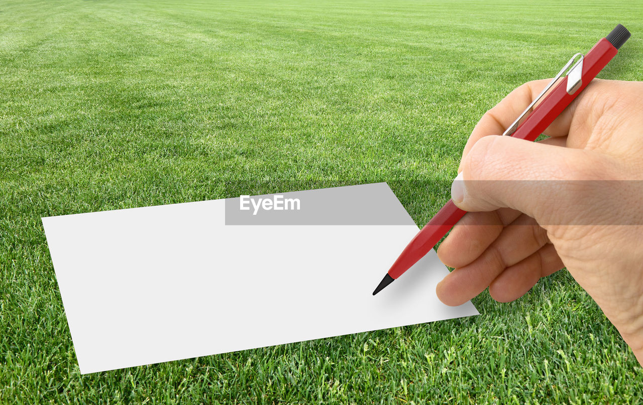 CROPPED IMAGE OF PERSON HOLDING PAPER AGAINST GREEN GRASS