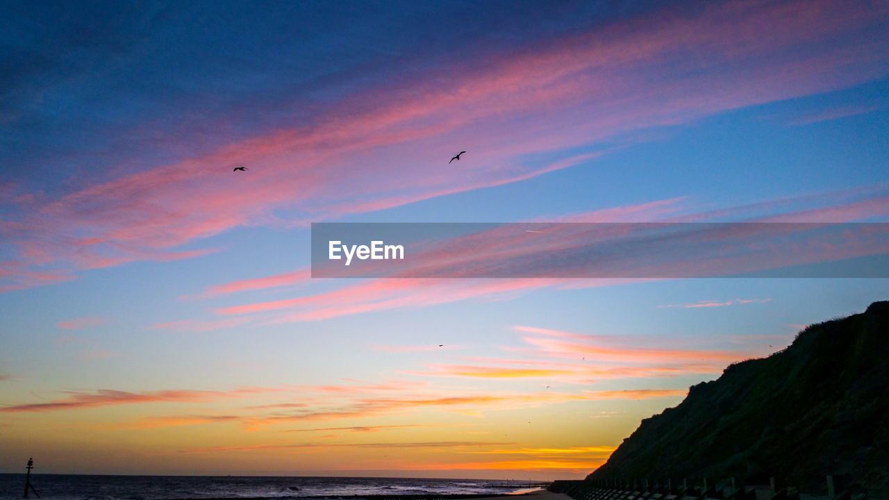 SCENIC VIEW OF BEACH AGAINST SKY AT SUNSET