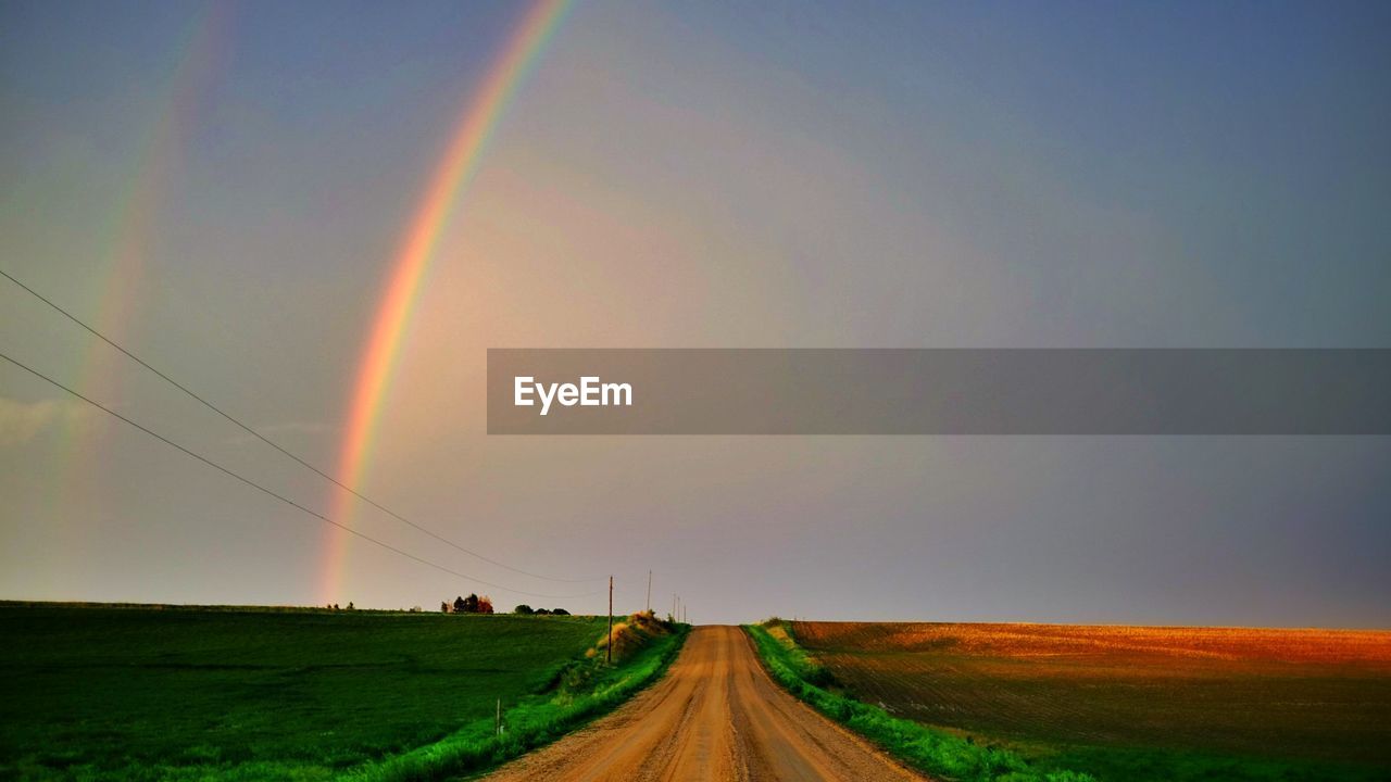 Narrow country road along landscape and against rainbow