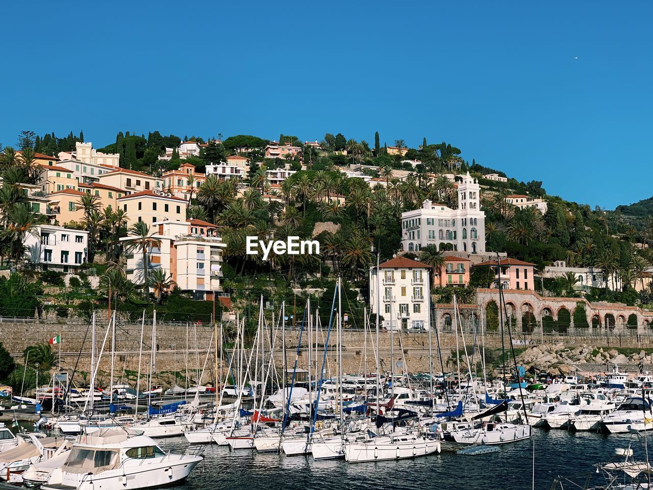 SAILBOATS MOORED AT HARBOR AGAINST BUILDINGS IN CITY