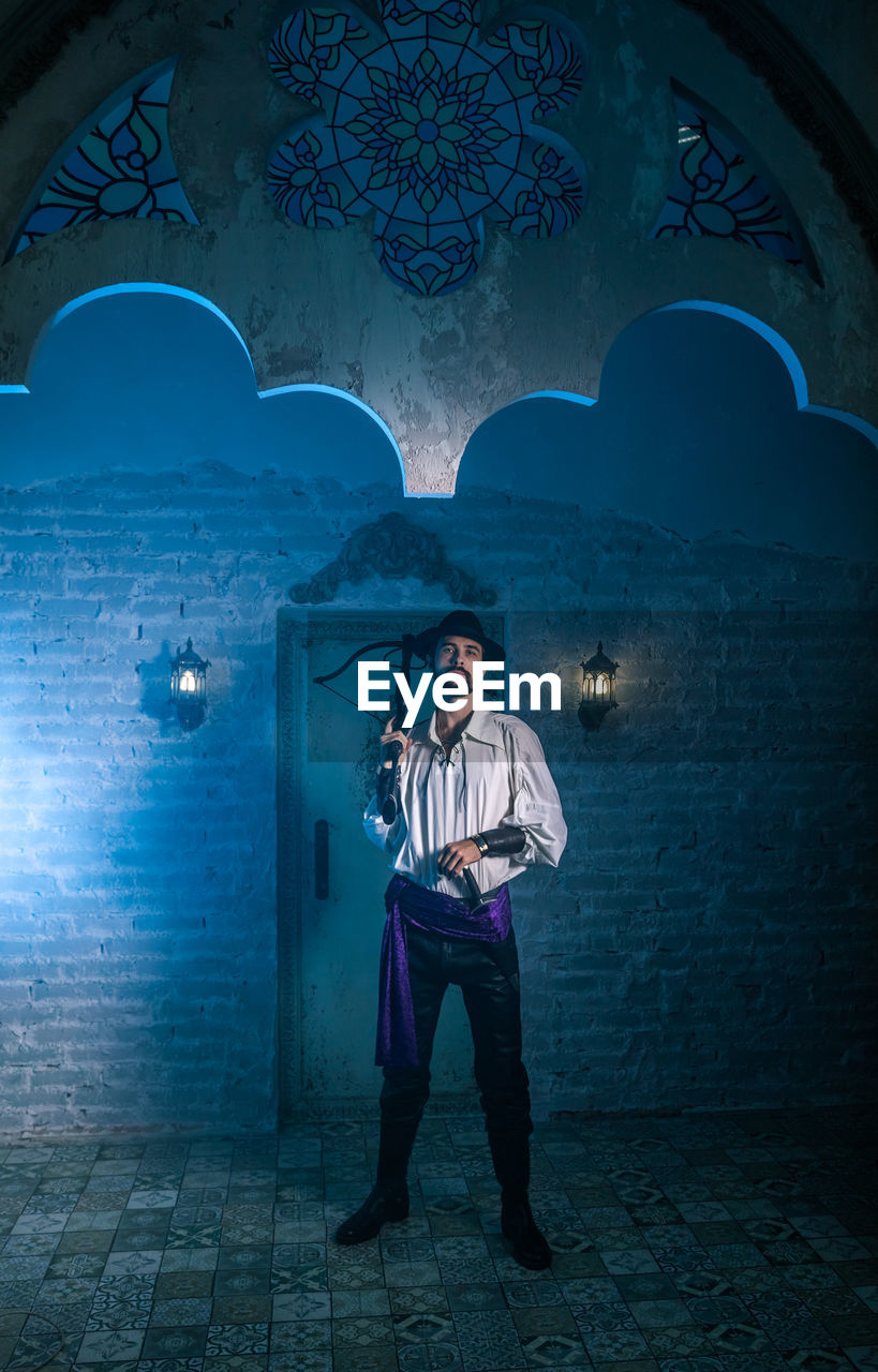 Portrait of man in costume standing against door of abandoned building at night