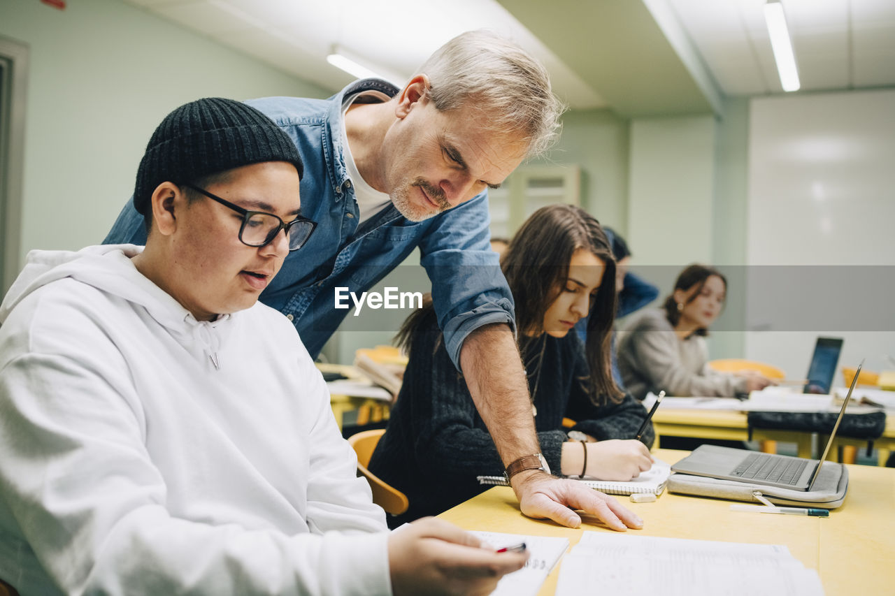 Male teacher assisting student at desk in classroom