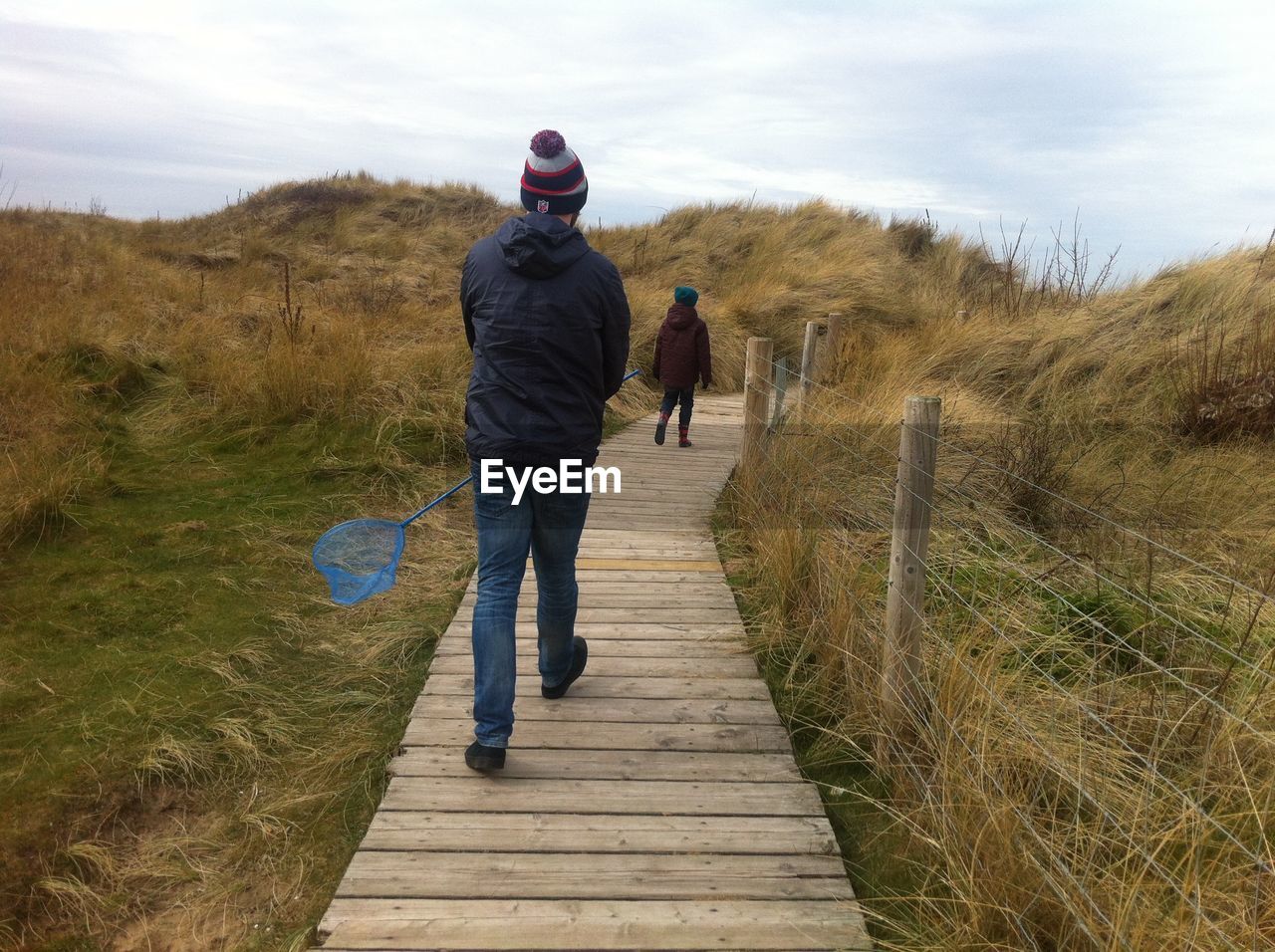 Rear view of man with butterfly net walking on boardwalk