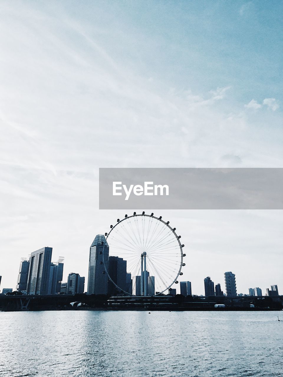 Low angle view of ferris wheel and buildings by river against sky