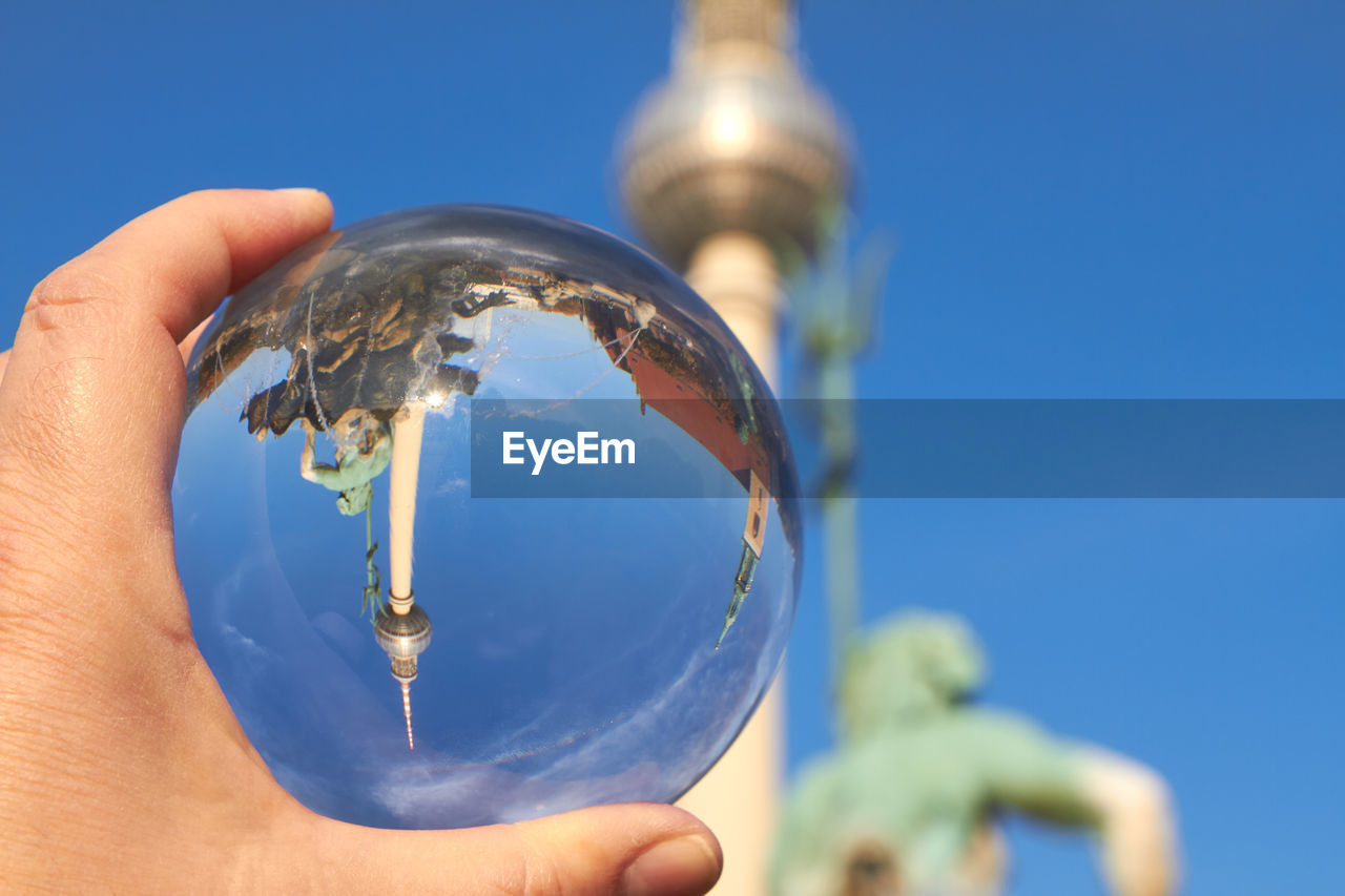 Cropped hand holding crystal ball against fernsehturm