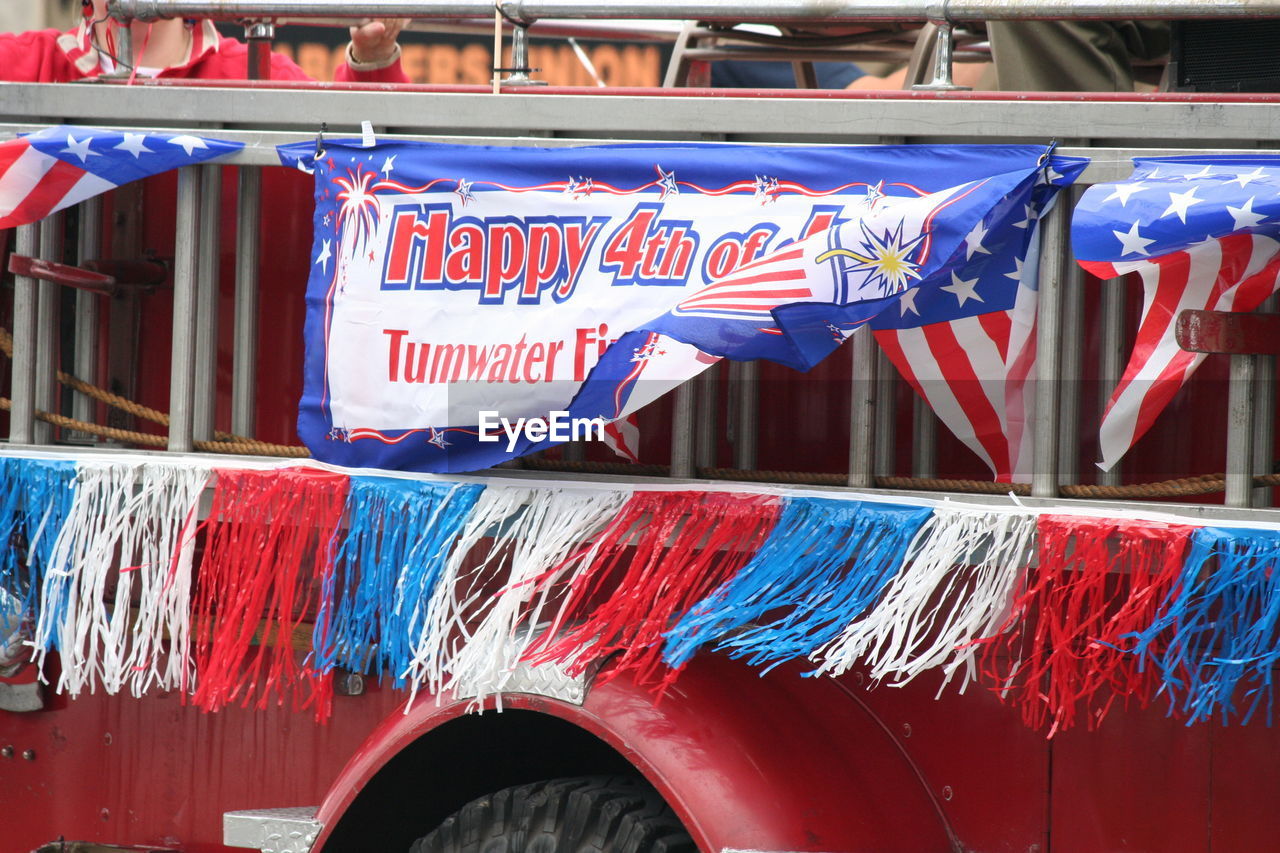 Banner with text on vehicle trailer over street during fourth of july parade
