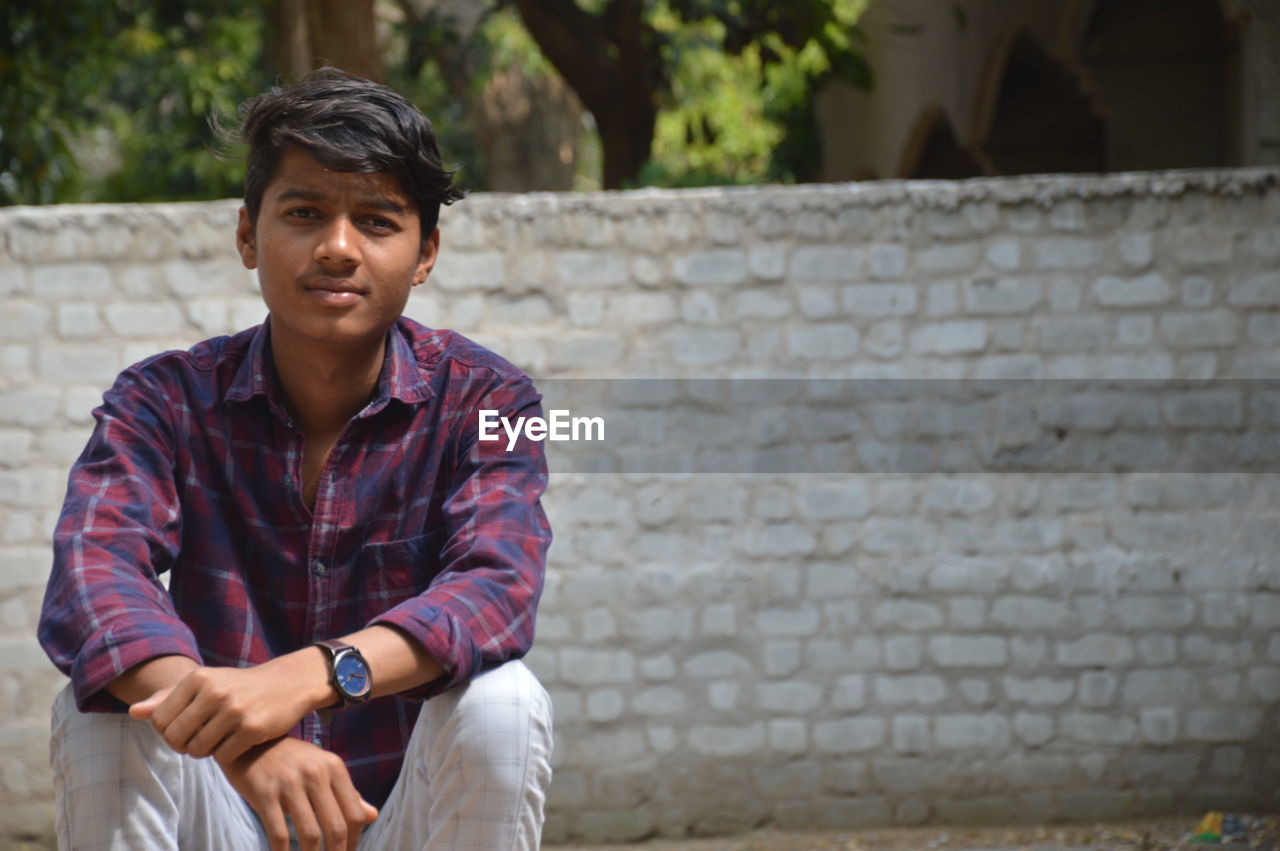 Portrait of young man sitting against wall