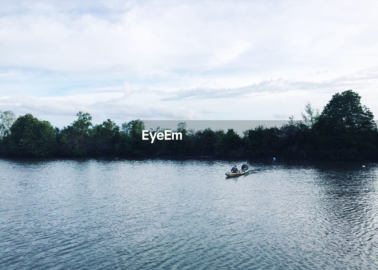 Man sitting on boat in river against cloudy sky