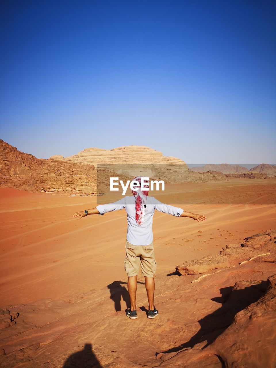 Rear view full length of man with arms outstretched standing at desert on sunny day