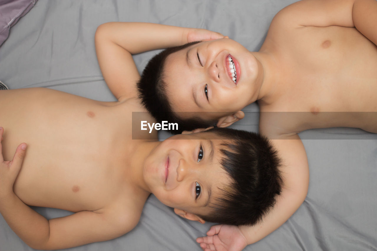 Portrait of shirtless boy with cute brother lying on bed