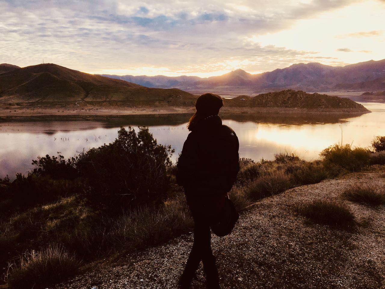 Rear view of woman standing on mountain against sky with view of lake