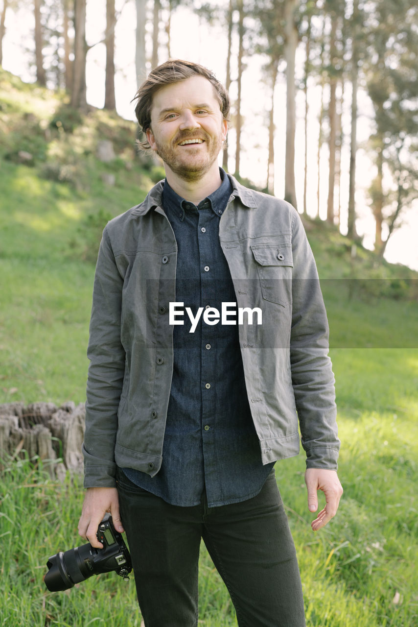 Man smiling outdoors looking into camera in casual dress with camera