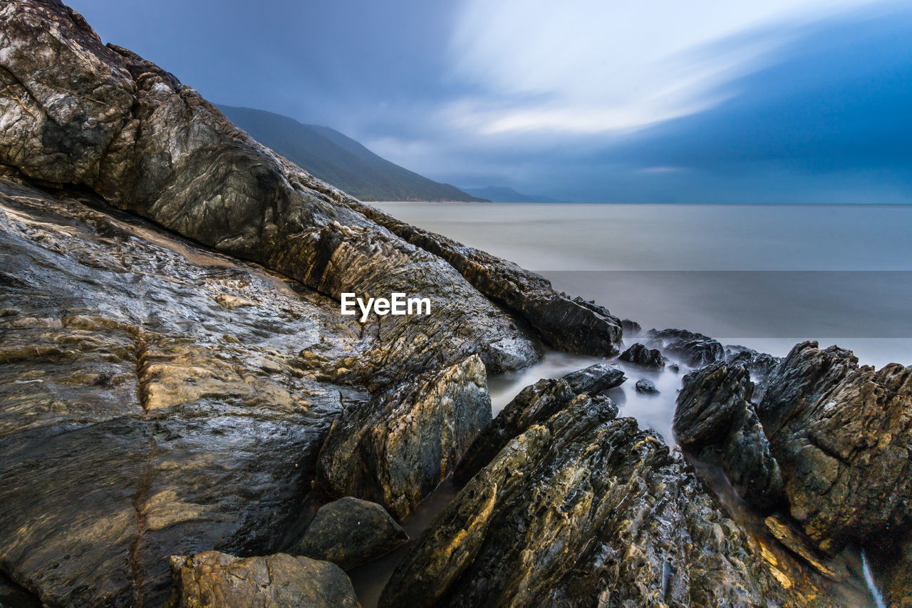 Scenic view of sea by rock formations against cloudy sky