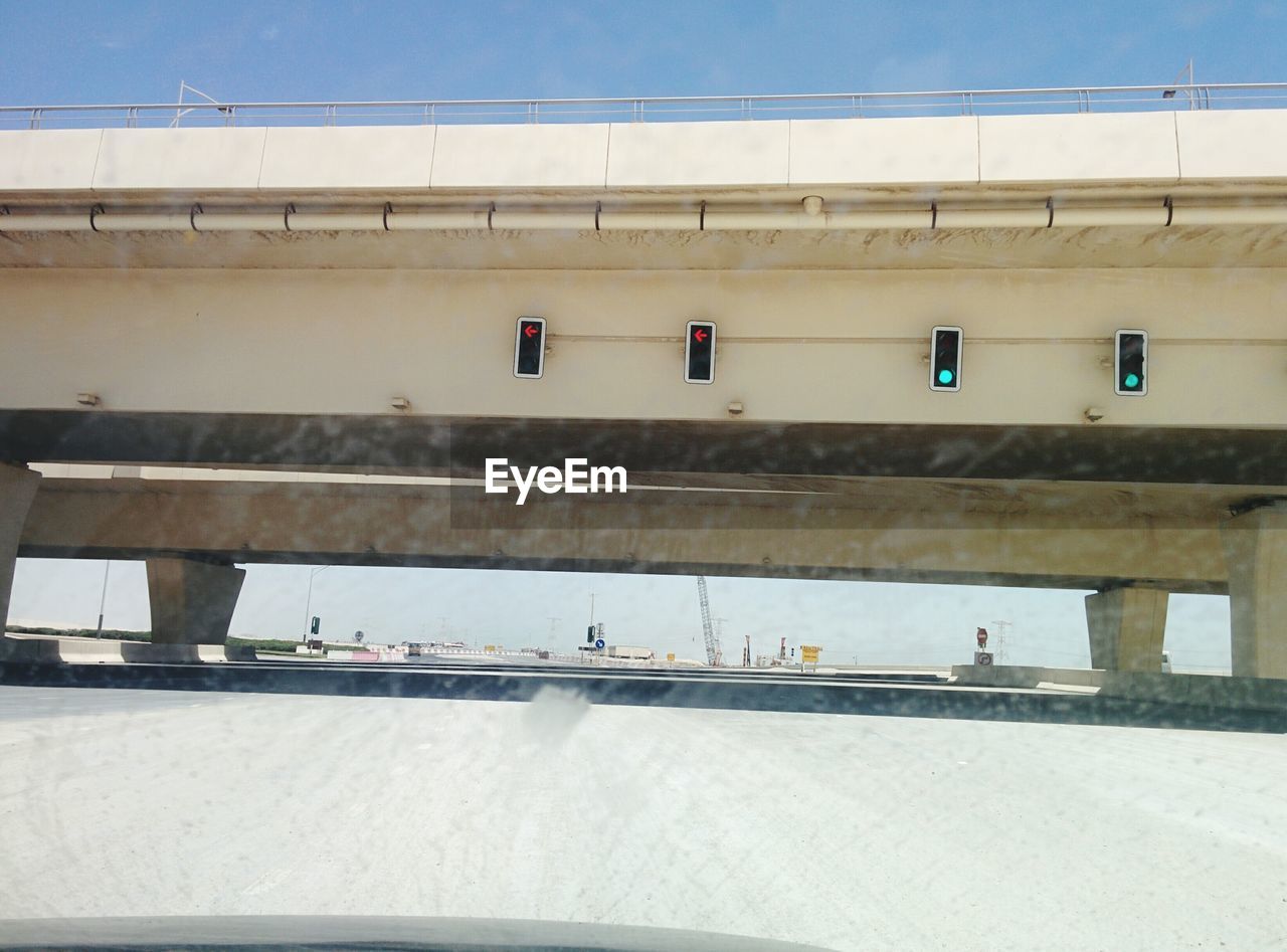 Stoplights on bridge over road seen through windshield