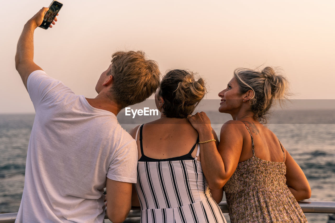 Beautiful mother with her twenty year old sons take a selfie by the sea at sunset. summer concept