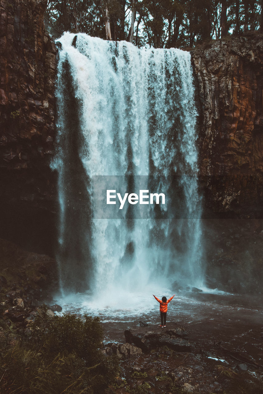 Scenic view of woman standing by waterfall