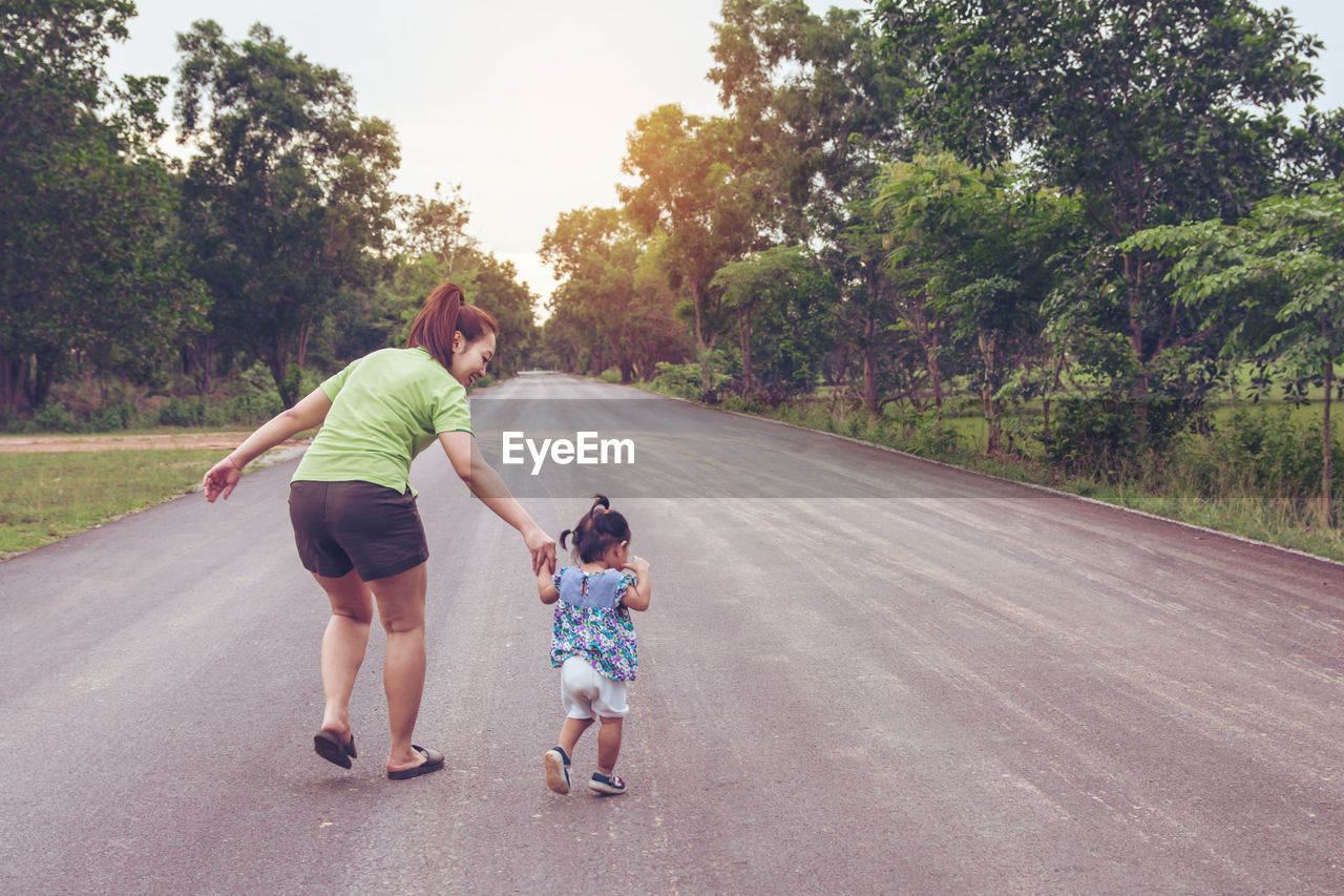 Rear view of woman with daughter walking on road amidst trees