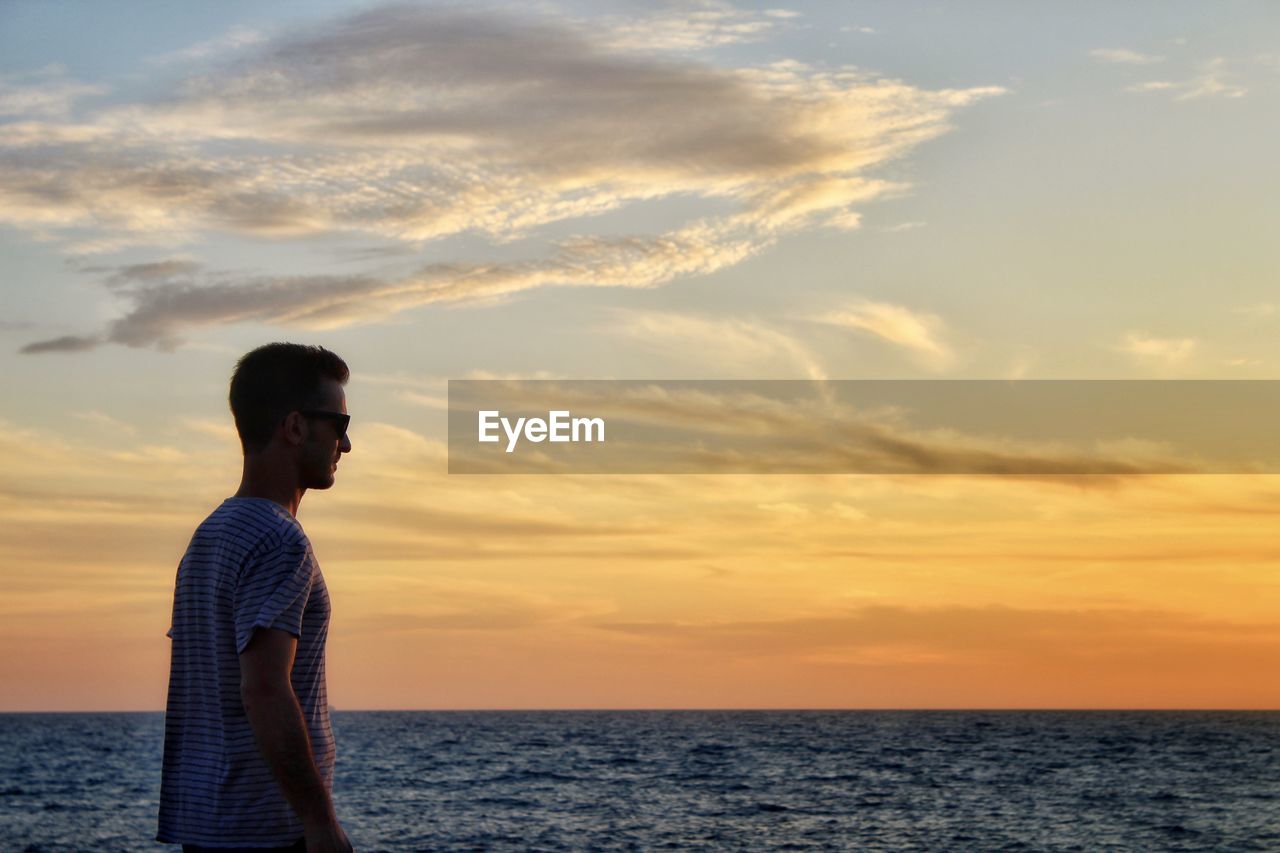 Man standing by sea against sky during sunset