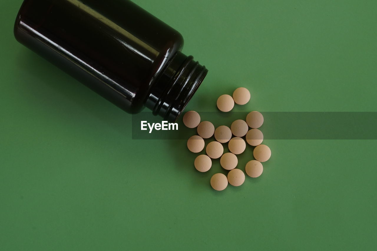 Close-up of pills spilling from bottle against green background