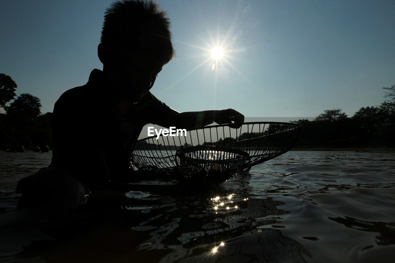 SILHOUETTE MAN IN LAKE AGAINST SKY