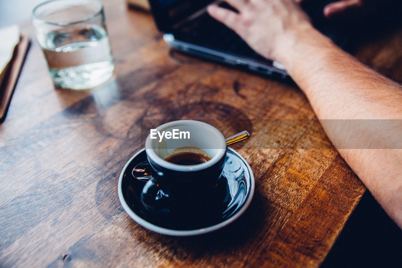 Close-up of coffee cup with man working on laptop