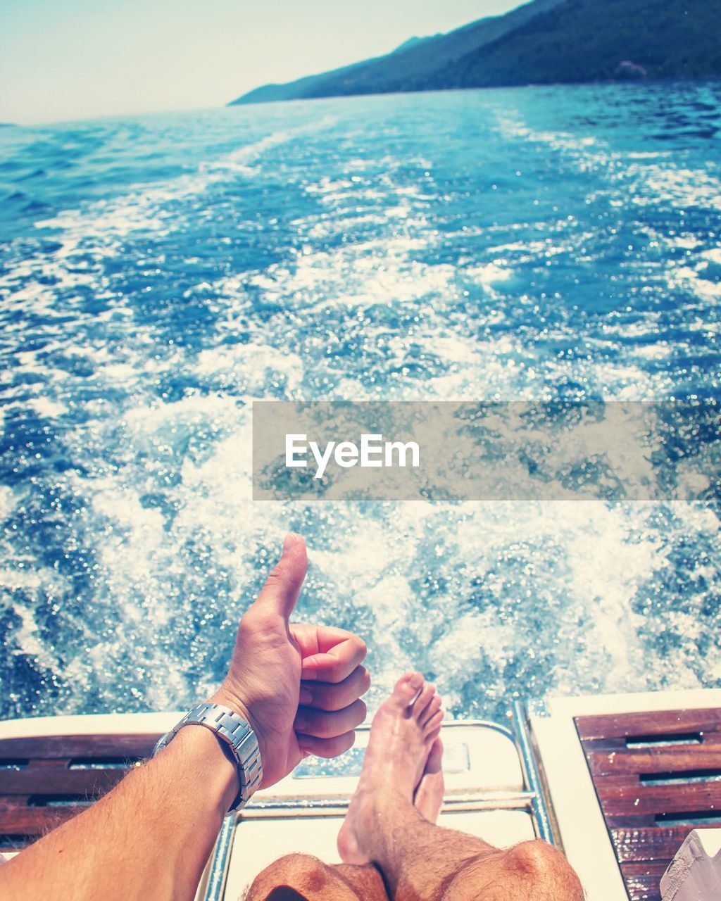 Low section of man showing thumbs up while traveling in boat on sea