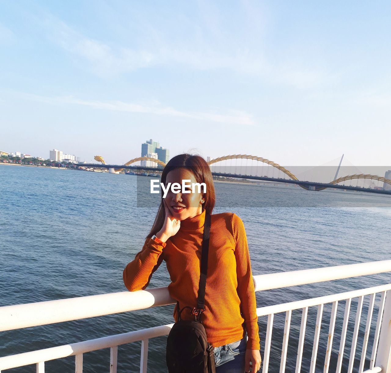 Young woman standing by railing against bridge against sky