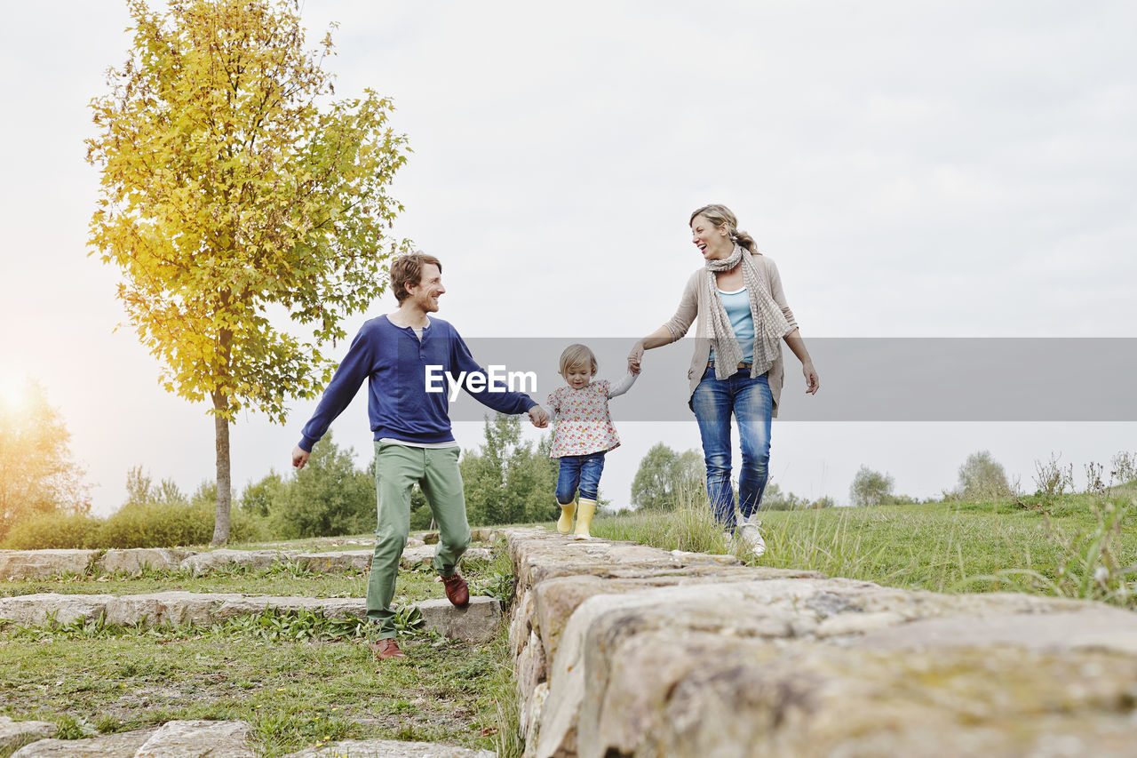 Girl balancing on a wall supported by parents