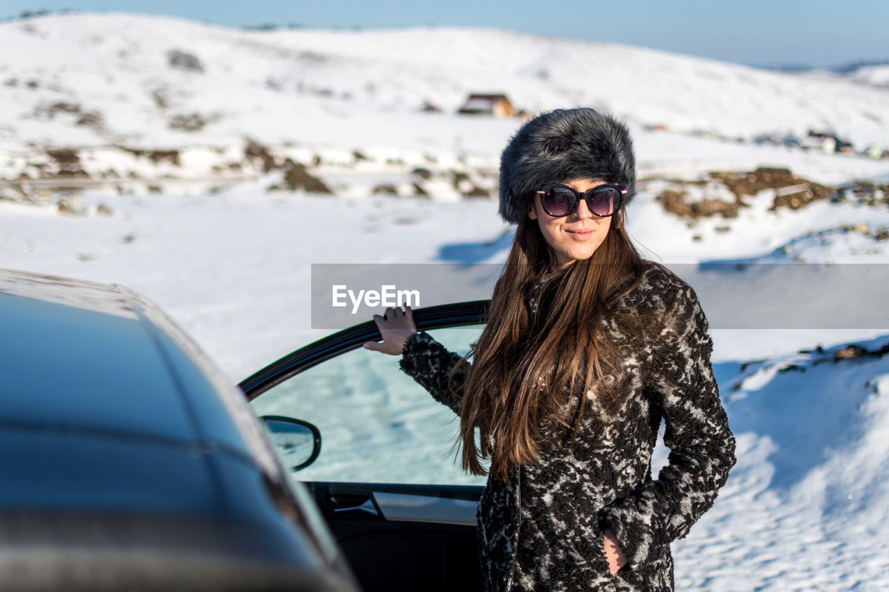 Portrait of woman standing by car on snow covered land