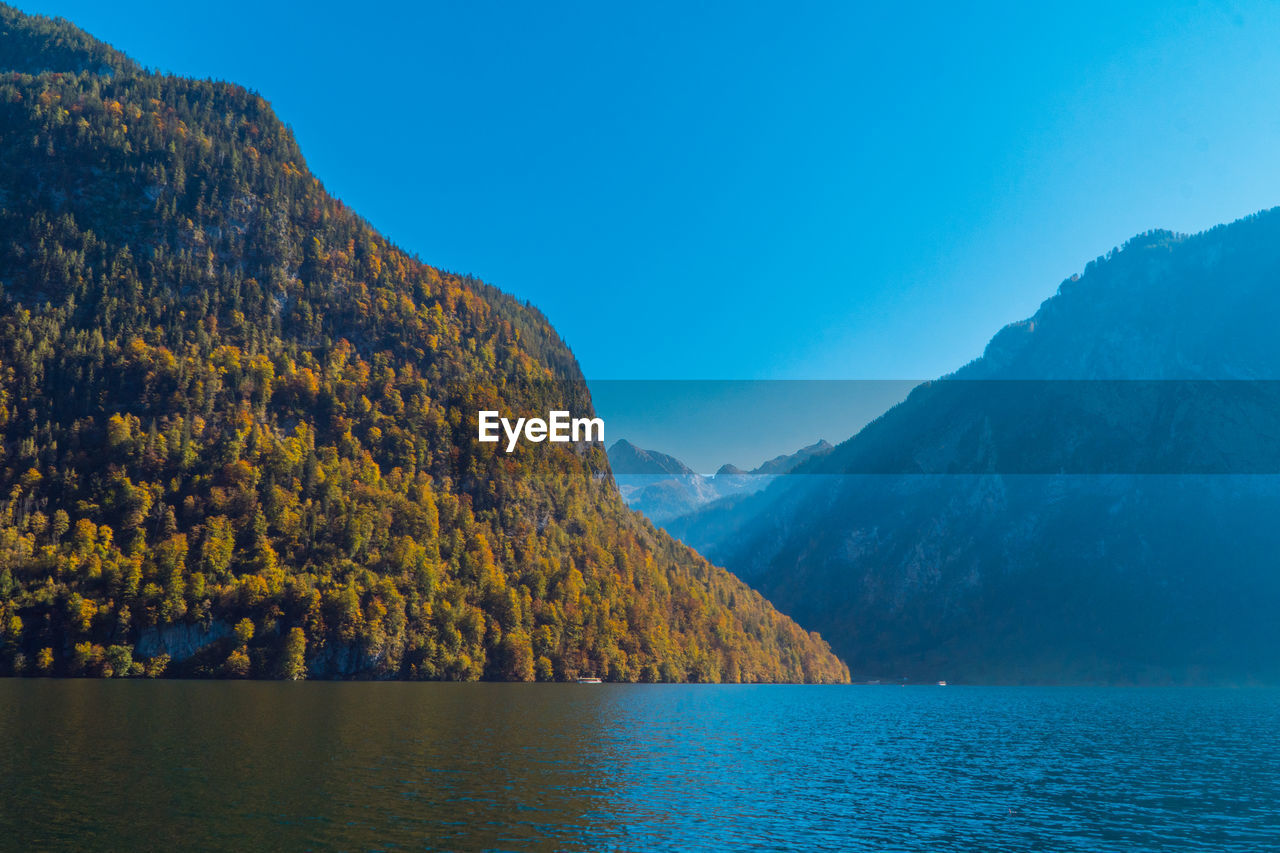 Scenic view of lake by mountains against blue sky