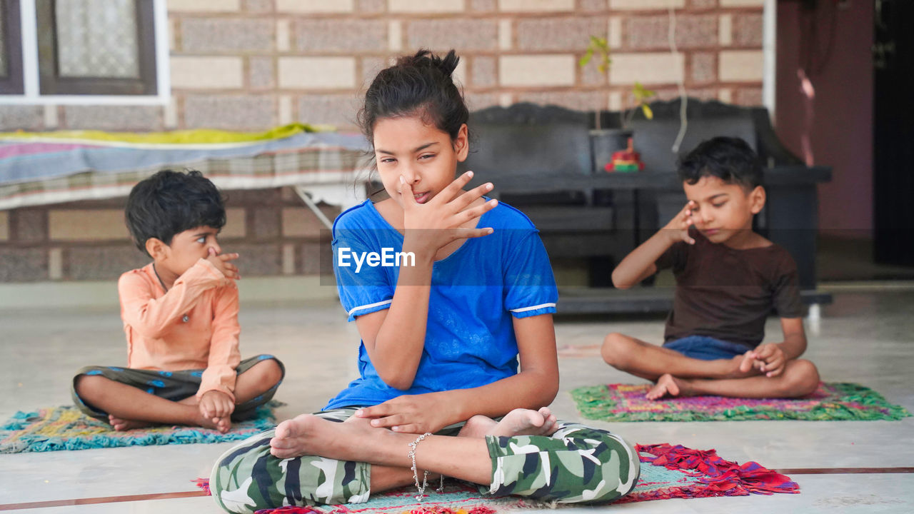 Group of children engaged in yoga at home sitting on the mat.