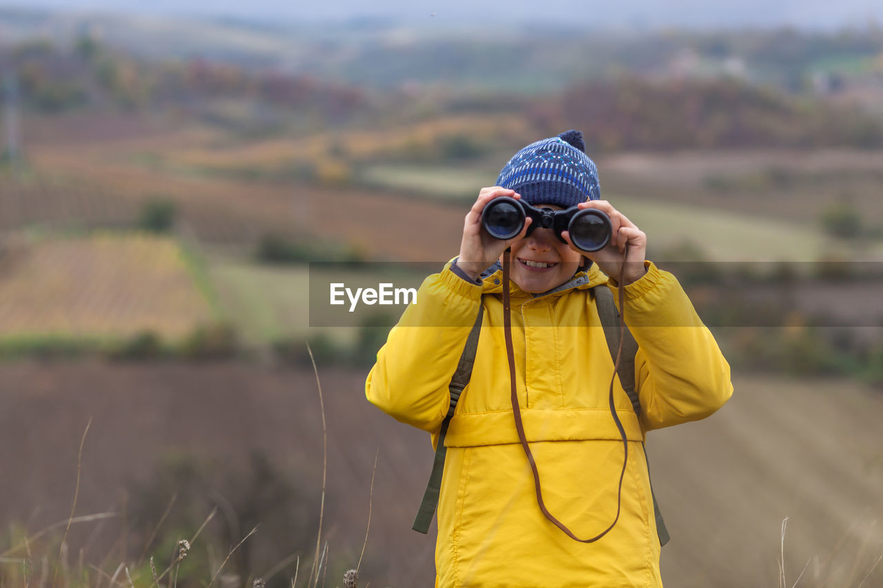 Happy little boy looking through binoculars during autumn day on a hill. copy space.