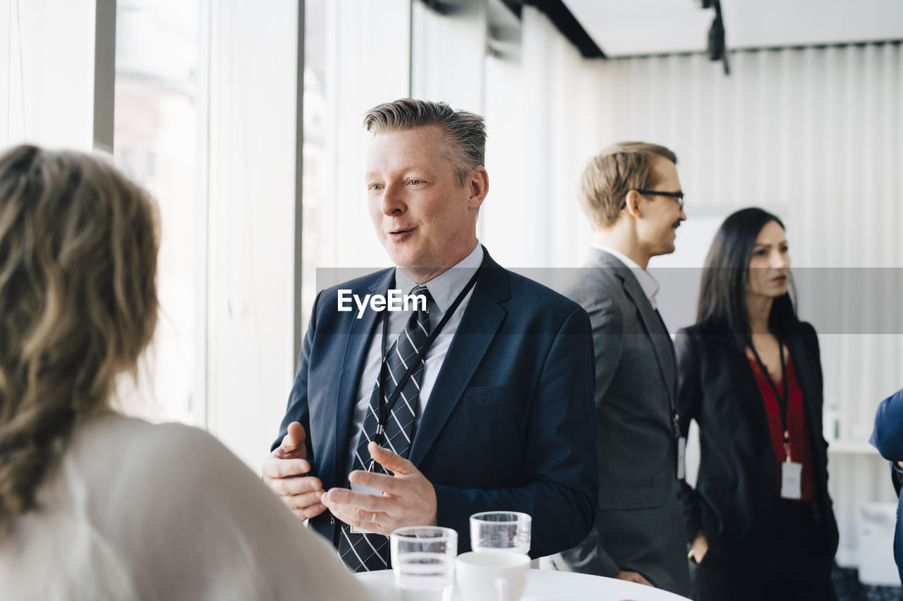 Male entrepreneur talking to colleague while coworker standing in background at workplace