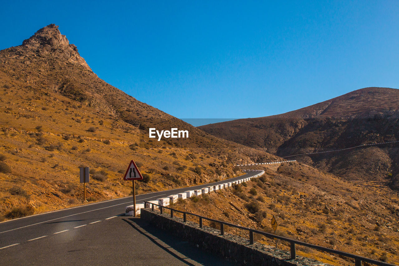Road leading towards mountain against clear blue sky