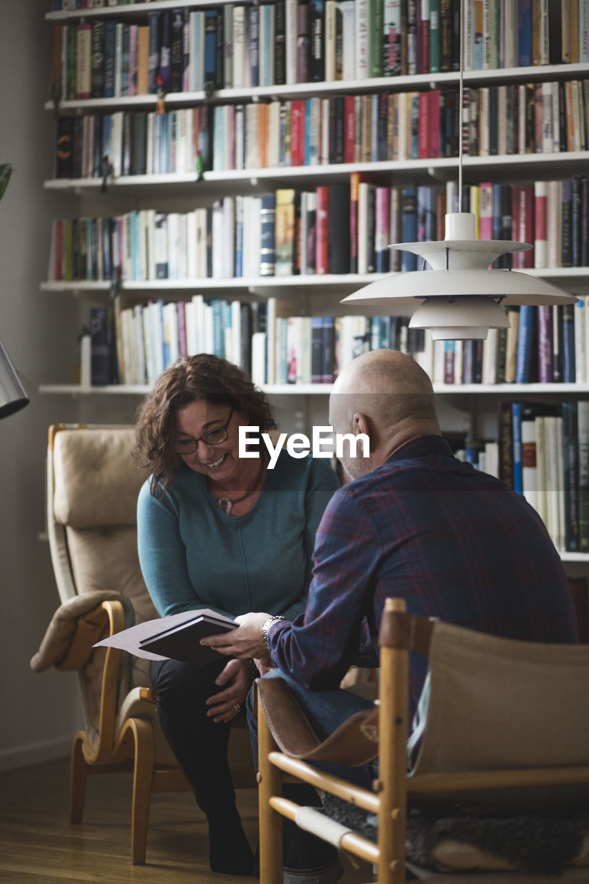 Male therapist showing document to smiling patient at home office