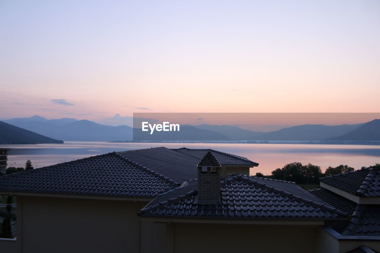 HOUSES BY SEA AND MOUNTAINS AGAINST SKY DURING SUNSET