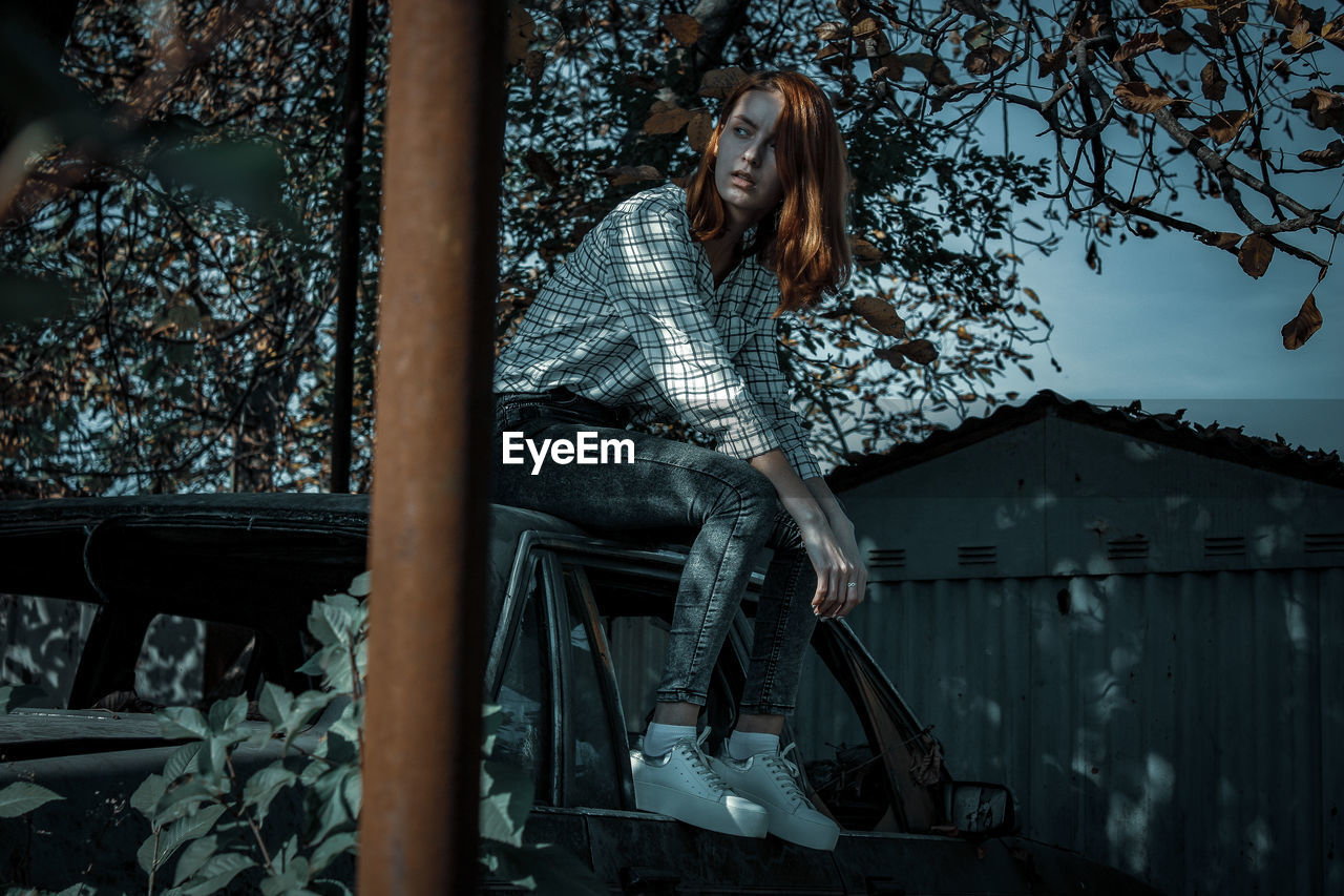 Contemplating young woman sitting on car