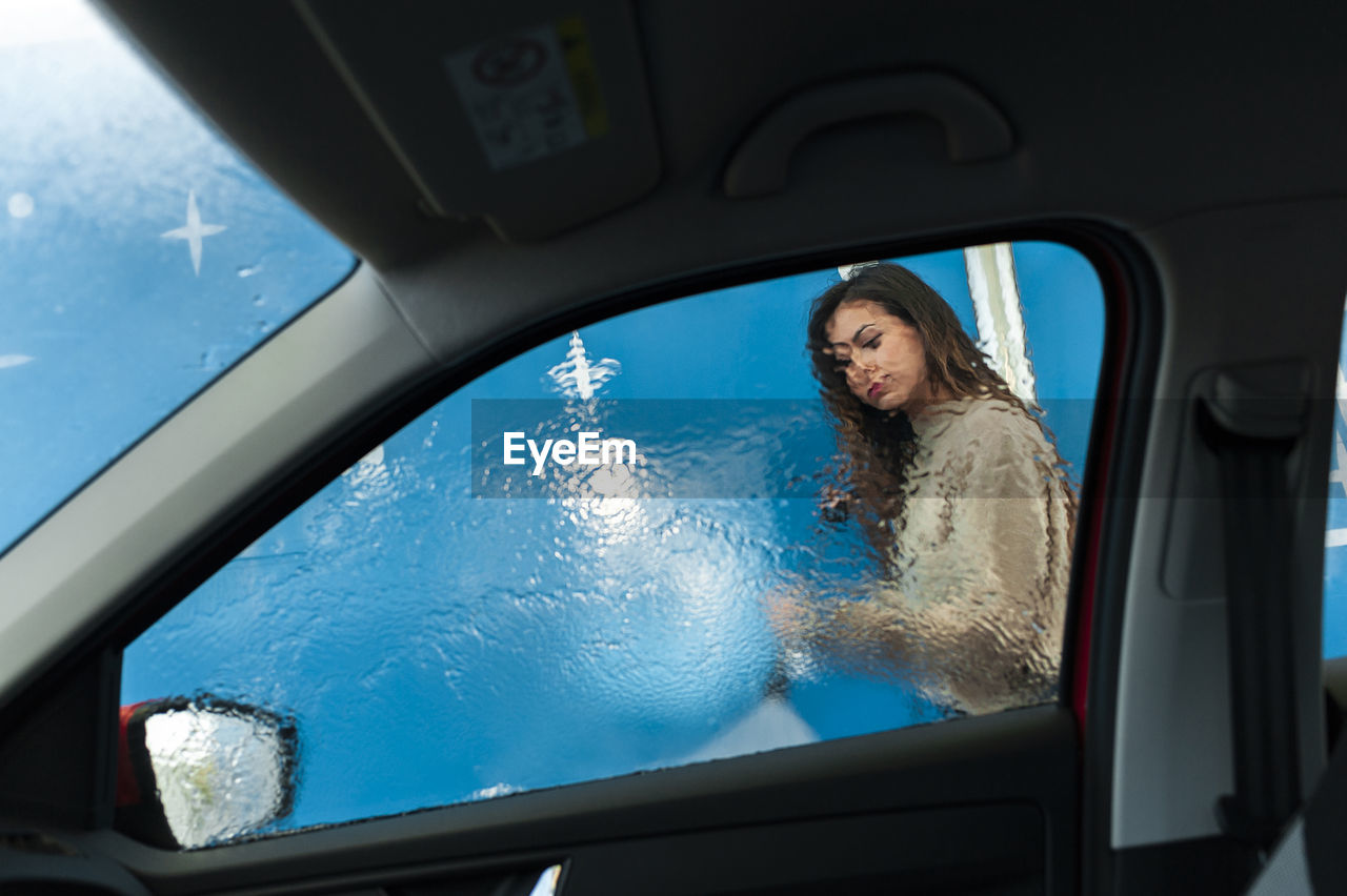 Young woman spraying water on window at car wash